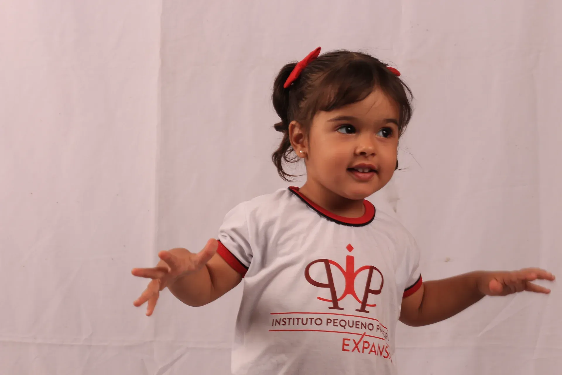 Criança do maternal de braços abertos, sorrindo, de camiseta do IPP no ensaio da campanha