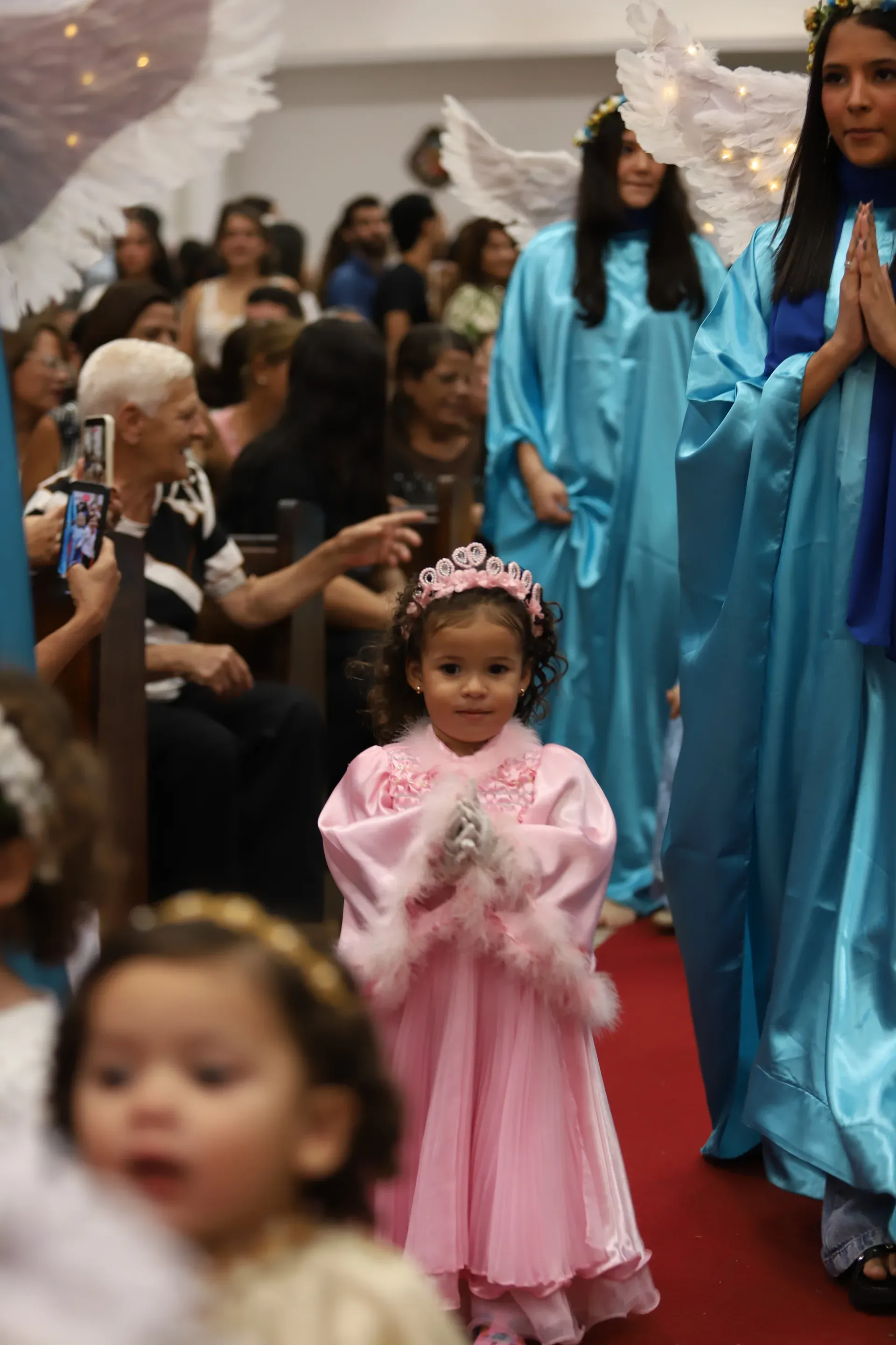 Meninas vestidas de princesa, de rosa e coroa, caminhando pela passarela da Coroação