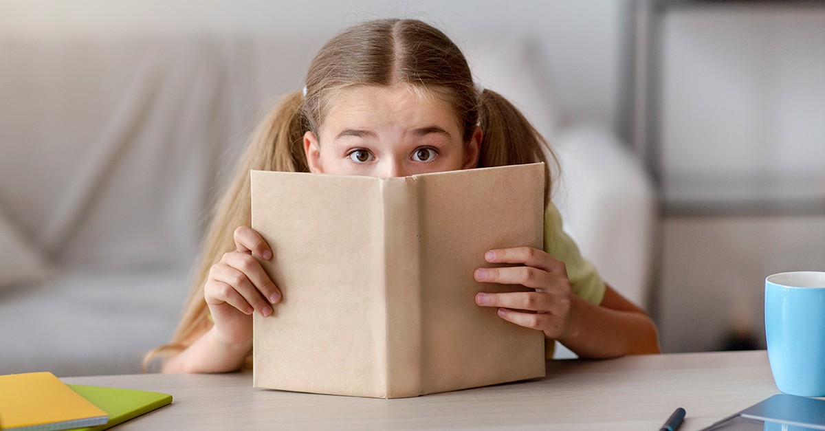 Criança tímida se escondendo atrás de um caderno